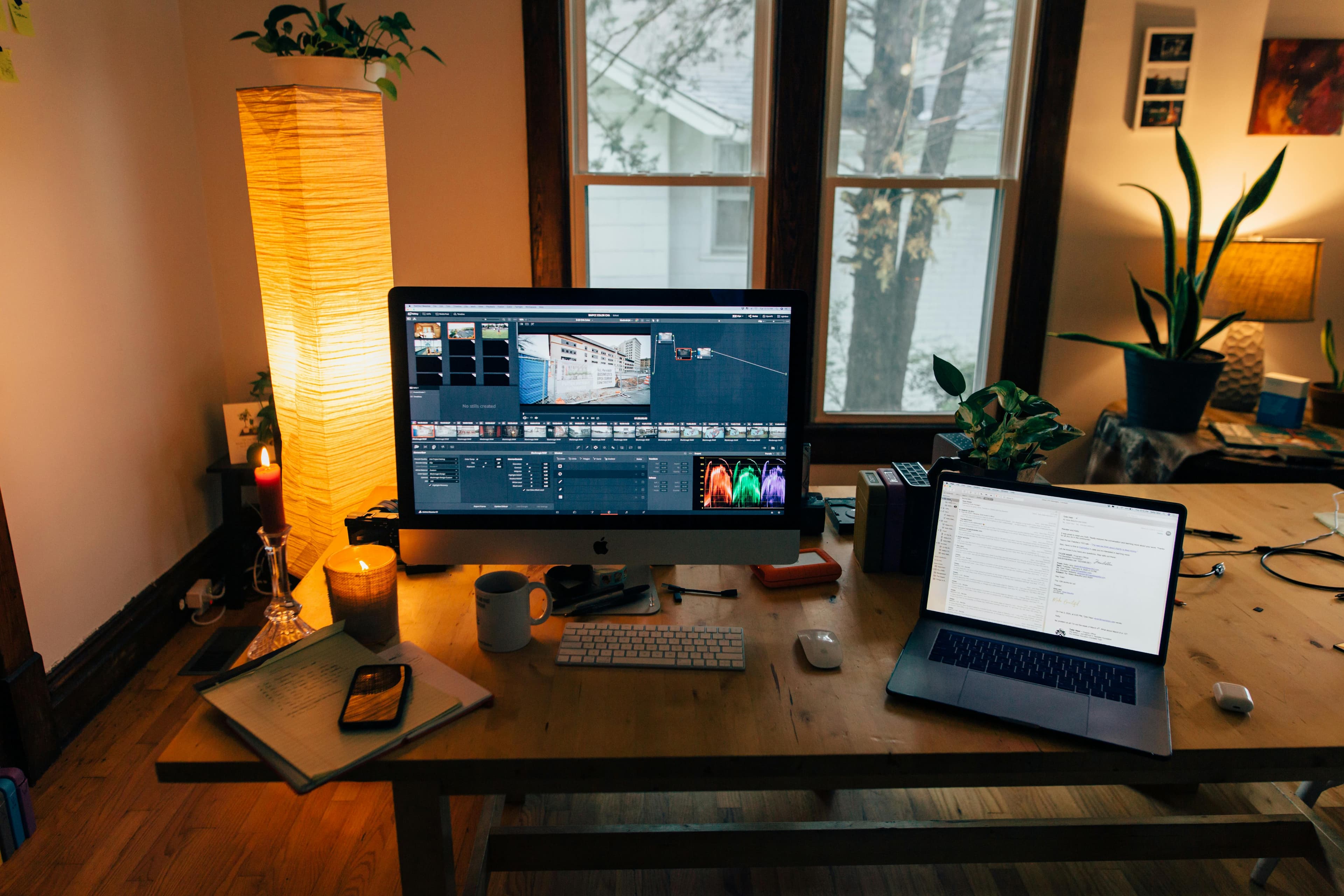 A cozy home office with warm floor lamp, iMac, MacBook, and natural window light layered together