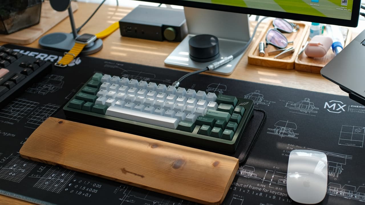 A mechanical keyboard on a clean home office desk with a monitor in the background