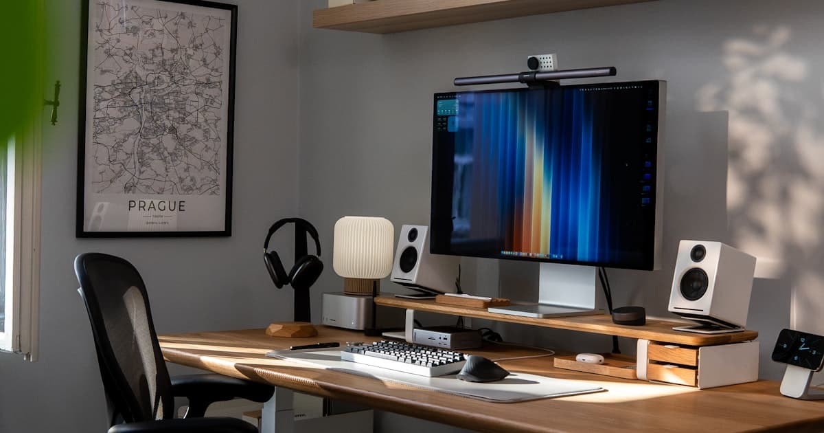 A modern home office desk setup with a monitor, plants, and tech accessories on a clean wooden workspace