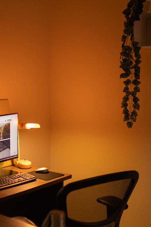 A cozy home office with warm layered lighting from a desk lamp and ambient sources creating a well-lit workspace